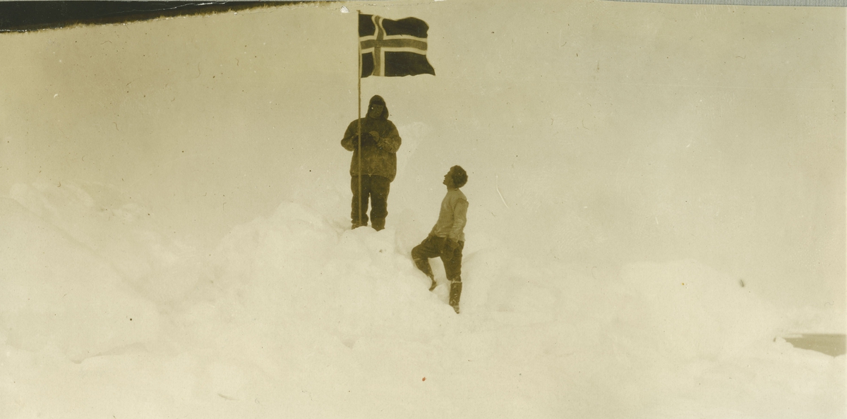 To menn i sneen med det norske flagget. Antagelig på en av Amundsens ekspedisjoner.