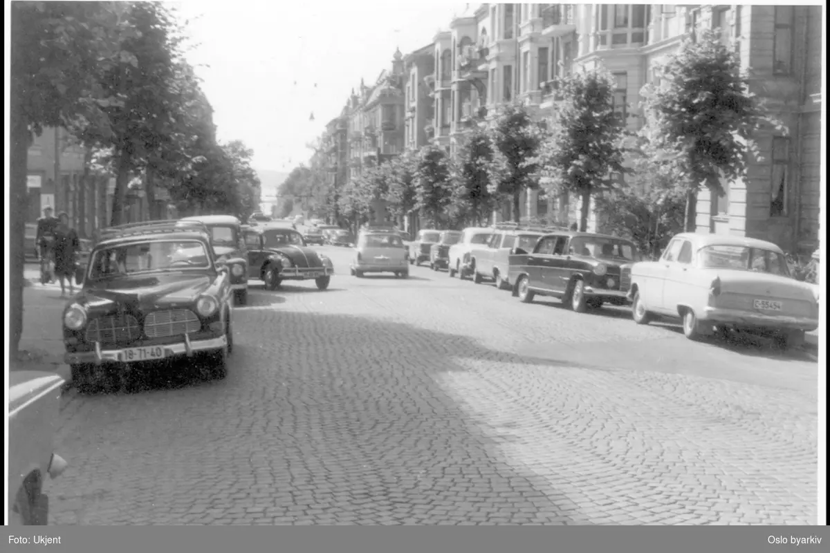 Nils Juelsgate. Brolagt gate med alle-trær. Folkevognen svinger ut fra Berens gate. Parkerte biler langs fortauskant på begge sider. Sannsynlig fra 1960-tallet.