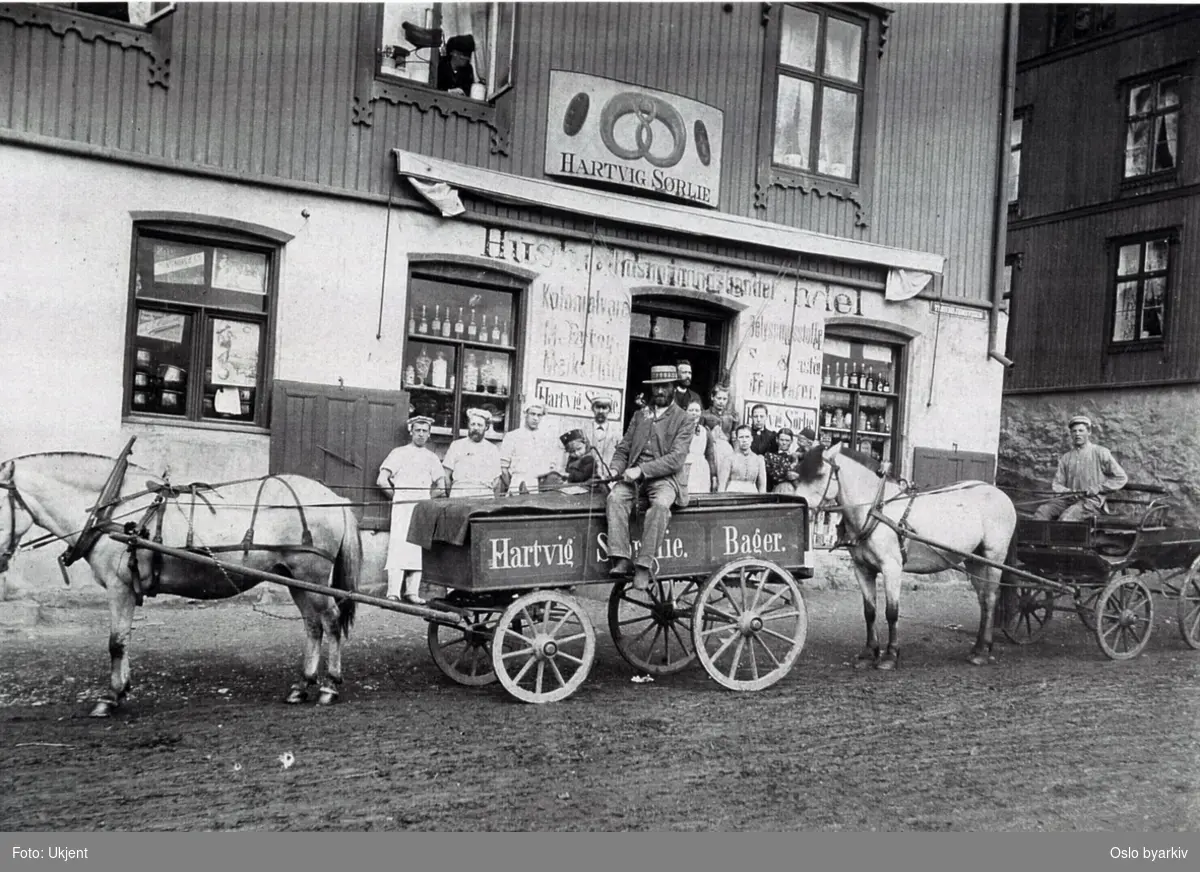 Baker Hartvig Sørlie med personale oppstilt på gata utenfor bakeriet. Hest og kjerrer utenfor Trondheimsveien 78. Butikkskilt.