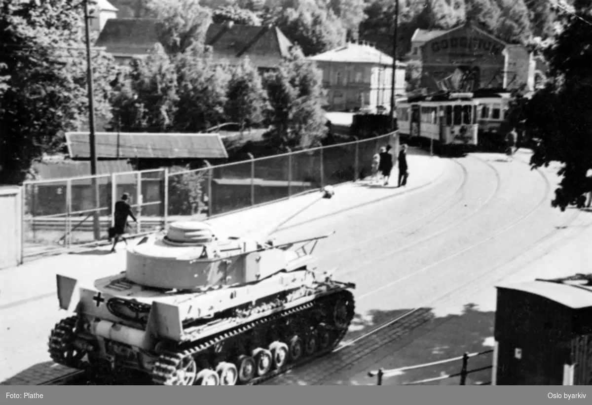 Tysk stridsvogn kjører langs trikkelinje i Oslo gate ved broovergang for jernbanelinje. I bakgrunnen ser vi foten av Ekeberg. Bildet ble tatt illegalt under krigen, 1940-1945, av en privatperson ved navn Plathe.