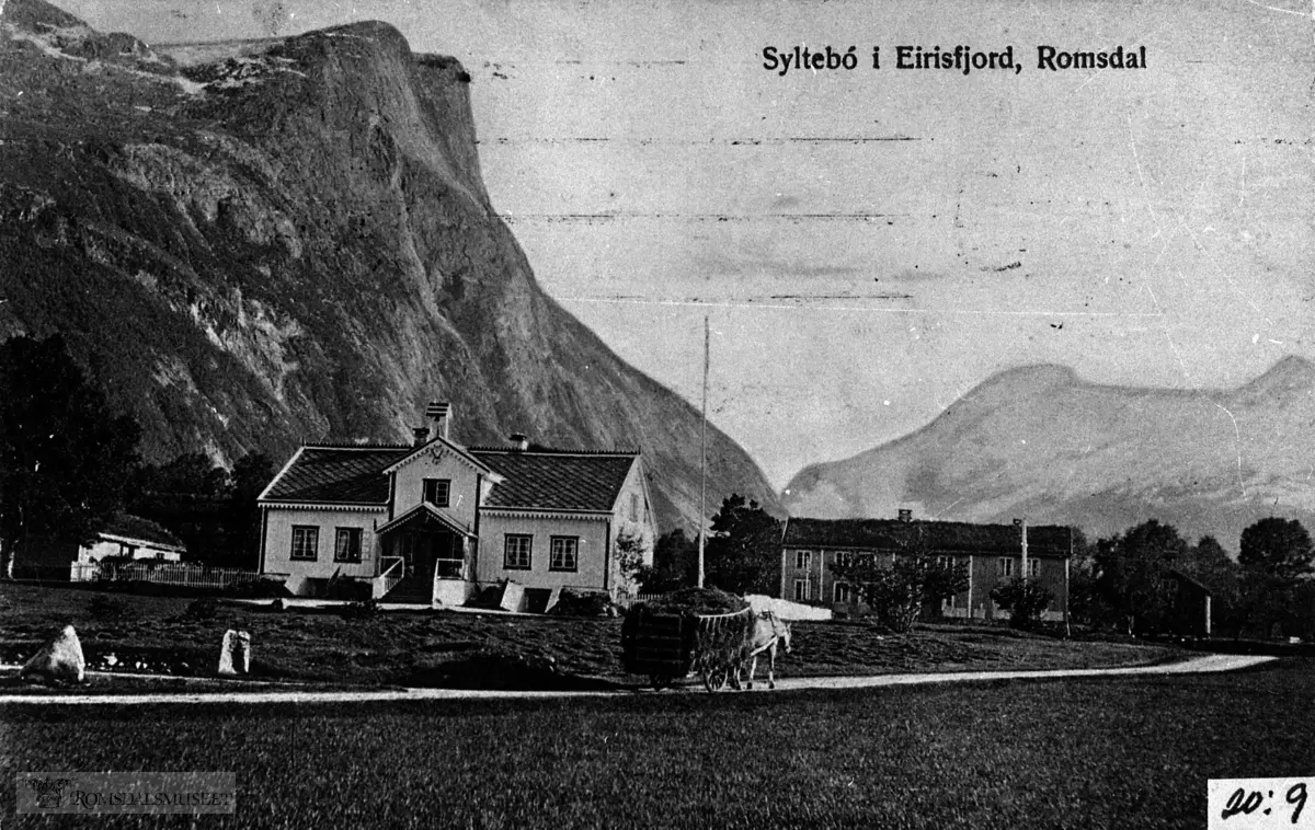 Syltebø i Eresfjord. Vi ser "Engelskhuset" frå 1864 og våningshuset på garden. Eit høylass blir køyrt forbi. ..I bakgrunnen Goksøyra. (Postkort stempla 23.12.1910.)..