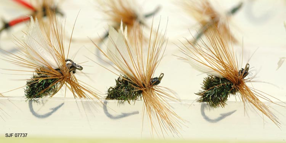 Tilstand: I forbindelse med omfototgrafering høsten 2002, oppdaget OT Ljøstad at enkelte av fluene i denne esken var totalt ødelagt av møllangrep.  Problemet må ses i sammenheng med at materialet har vært oppbevart i magasin C, der temperaturforholdene har passet møllen godt.  Fluene vil nå bli reingjort og flyttet til kjølerommet. 

Boksen inneholder ialt 76 fluer alle ant. tørrfluer. 2 stk har ekstra lange bein ant. navn: Daddy long legg. Tørrfluene virker på den måten at de flyter oppå vannet. Giveren har skrevet ei bok som heter "Isfiske" sammen med Knut Rom, boka ble utgitt i 1972. Giverens far var en ivrig sportsfisker og er gitt tittelen "Den fullendte sportsfisker". 