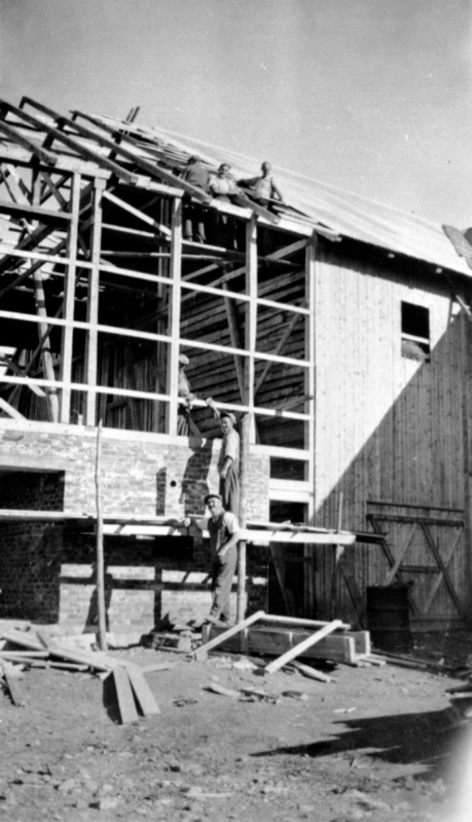 Bygging av ny låve på Skjønsby gård, Ringsaker. Snekring, reisverk. Folk som arbeider. Den første låven brandt ned høsten 1917. Andre brann 1937.