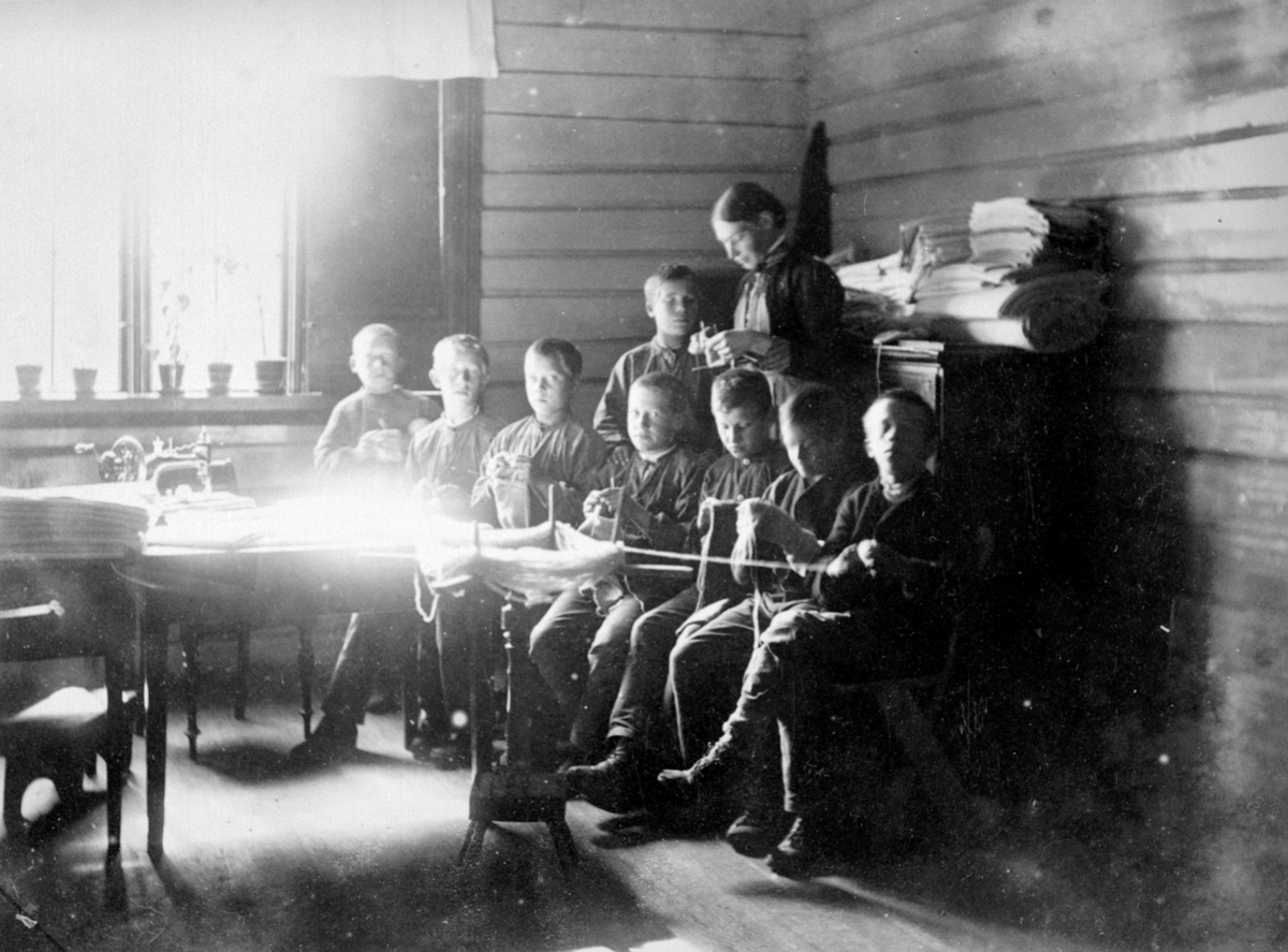 8 gutter strikker på systua på Toftes Gave, Nedre Sund, Helgøya. Lærerinne overvåker arbeidet.