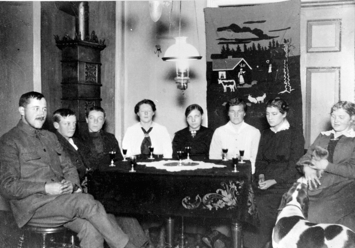 Gruppe personer rundt et bord. Vinglass på bordet. Fra venstre er Even Mengshoel, Kristian Sveen, Hans Sveen, Marie Mengshoel, ukjent, ukjent, ukjent, Agnes Mengshoel.
