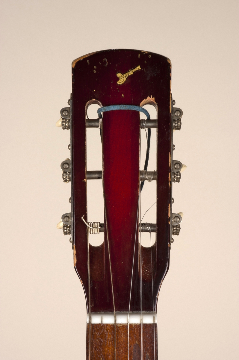 Akustisk gitar med rødmalt lokk med påført hvit skrift og gult plekterbrett. På gitarkroppens sider, hals og hode sees originallakk i sunburst. Fingerbrett i mørkt tre og sal i ben.