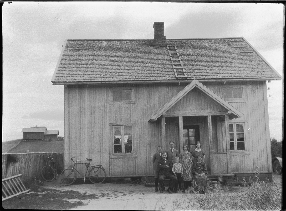 Ukjent familie ved inngangen til et hus. Sykler inntil husveggen. 
