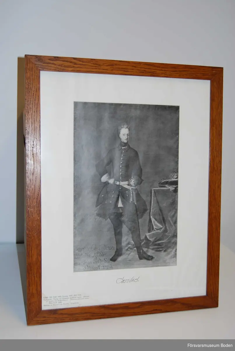 Inramad, avsedd att hängas på vägg. Svartvitt tryck av David von Krafts målning föreställande Karl XII i uniform från fälttåget år 1700. Med informationstext nertill i vänstra hörnet