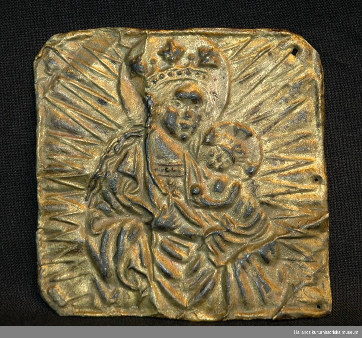 Förgylld kopparplåt med pressad bild av madonnan och barnet omgiven av en strålgloria. Tre hål i plåtens högra sida.