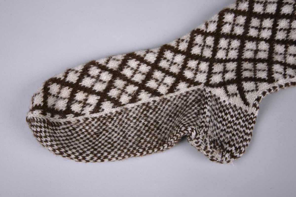 Lange strømper i glatt mønsterstrikk med ribbet kant øverst. Rutete mønsteri hvitt og brunt. Ett par.