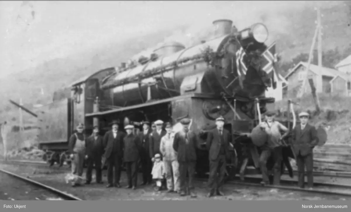 Et flaggpyntet damplokomotiv type 31b nr. 427 med både jernbanepersonale og sivile oppstilt foran lokomotivet