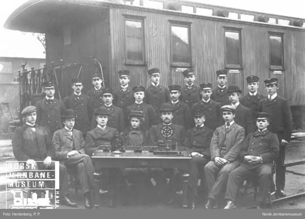 Gruppebilde med 22 telegrafistelever foran personvogn litra Co nr. 340 og bak et bord med telegrafiapparater
