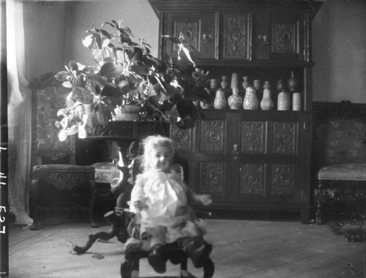 Interiør, Dal gård, Ullensaker. Rom med skap med keramikkanner(?) og dukke i stol.
Fra serie fotografert av kammerherre Fredrik Emil Faye (1844-1903), gårdens eier.
