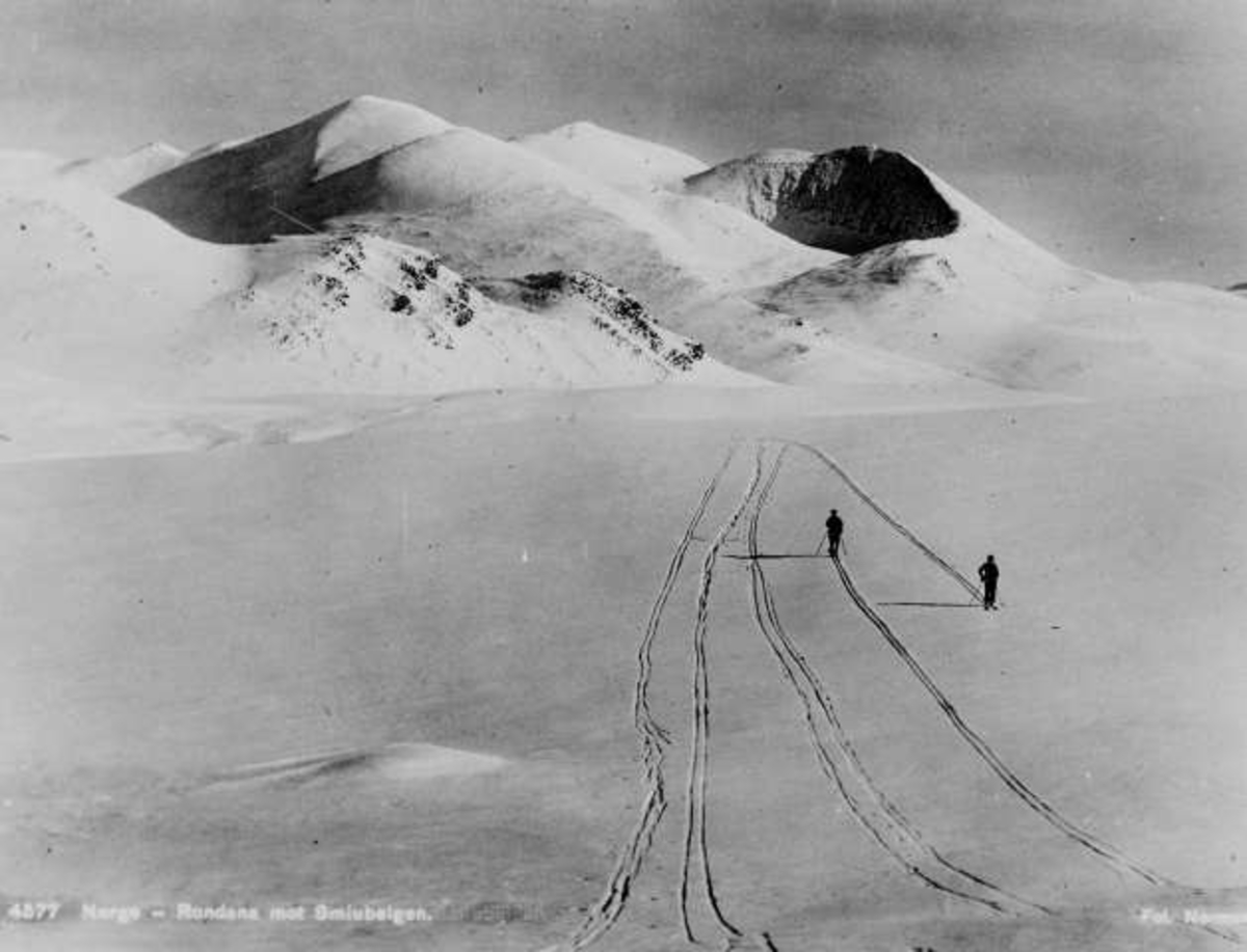 Avfotografert postkort. To skiløpere på vei hver sin vei i Rondane. Utsikt mot Smiubelgen i bakgrunnen.