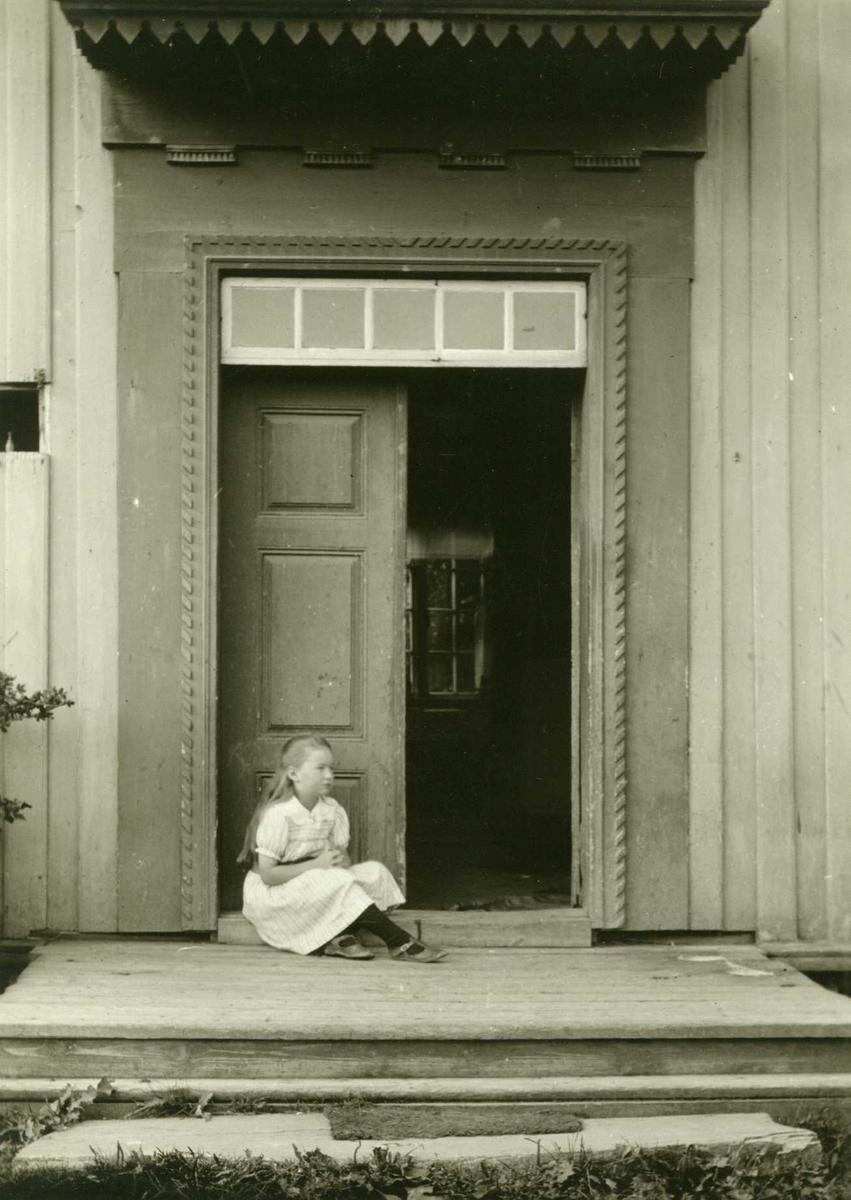 Kjøkkeninngang, Stiklestad prestegård, Verdal, Nord-Trøndelag. Jente sittende på dørstokken. Fotografert 1916.