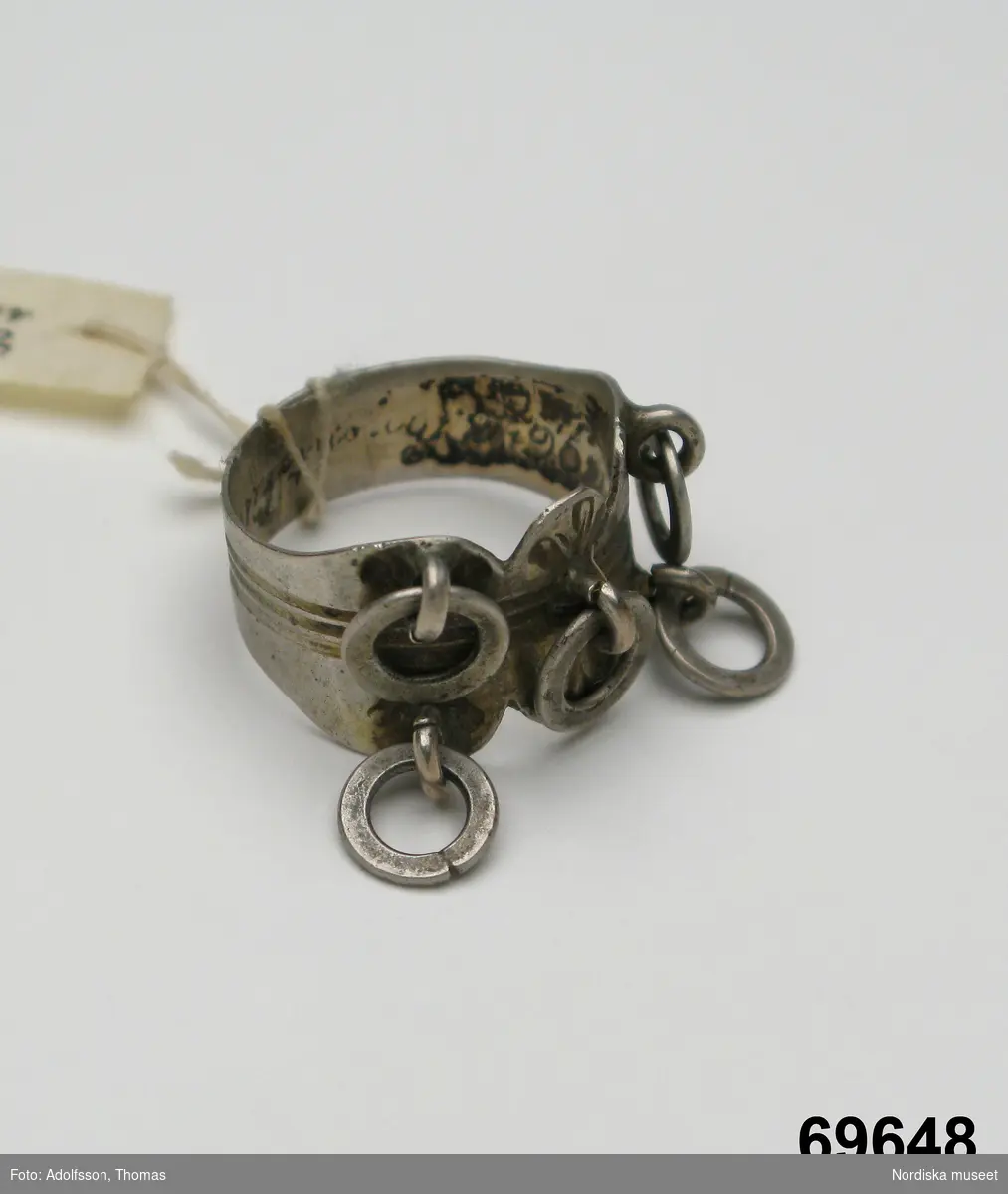 Huvudliggaren:
"Fingerring fr. Enontekis kapellförs., Finska lappmarken. Från Palojoki. Af silfver. Stämpl.: 'C N E 13 1/3.' Ink. fr. Köngämävuomalappen Per Andersson Valkeapää. Ink. af jägmästaren Hugo Samzelius. 1891. Bil. Samzelius 350."