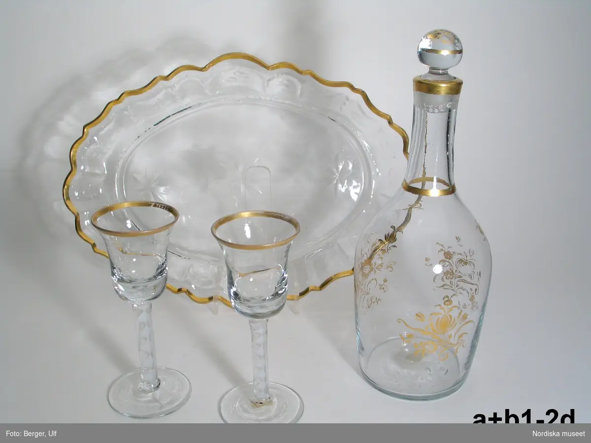 Huvudliggaren (år 1893):
"77286a-e Glasservis. Med schatull. 
a) Karafin. H. (m. propp) 0,265). Prydd med strödda blombuketter i guld; med kulformig glaspropp. 
b:1-2) 2 vinglas. H. 0,147. Klockformiga, på hög fot, incrusterade med hvitt, upptill med förgyld kant. 
c:1-2) 2 vinglas. H. 0,152. Kalkformiga, för öfrigt såsom b, men med olika incrustering. 
d) Bricka. L. 0,33. B. 0,238. Oval med utvikt krusad brädd och förgyld kant, i botten tre stjärnformiga ornament inslipade. 
e:1) Schatull. H. 0,155. L. 0,36. B. 0,267. Af trä, aflångt fyrkantigt, utvändigt klädt med brunt skinn, med 2 handtag af mässing. Å locket E. P. i monogram inprässadt. 
e:2) Hit [till schatullet] hör en senare sydd dyna klädd med svart sammet och grönt siden. 
Karafinen och 2 af vinglasen hafva antagligen icke ursprungligen hört till schatullet. Nyckeln till schatullet saknas. Ink. ss. 77251 [=å juvel. Chr. Hammers aukt. i Köln] = 17 Mk. Okt. 1893. Bil. Hammer 507."

Bricka med karaff och två glas. Troligen tillverkat i Tyskland ca 1760.
