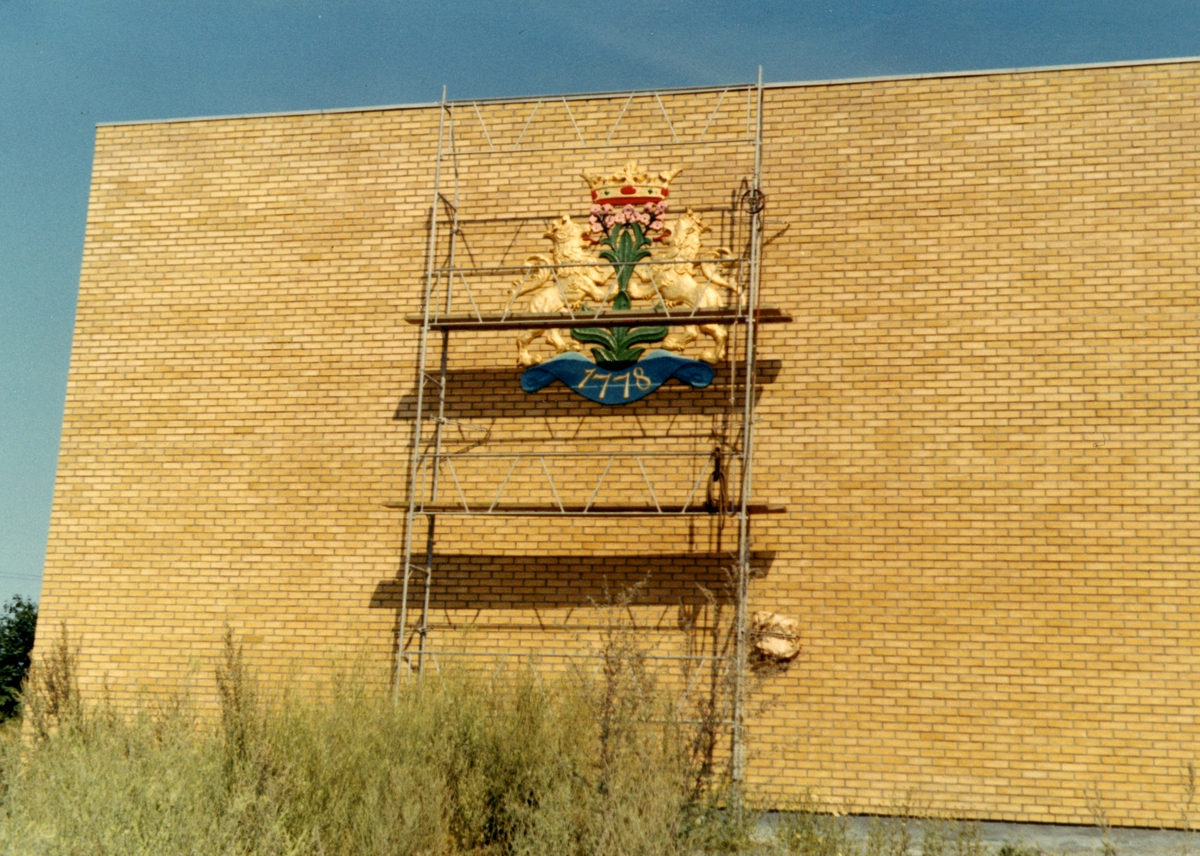 Byggeplass. 
Konstruksjon av Tiedemanns Tobaksfabrik på Hovin i 1968. En skilt forestillende Tiedemanns logo settes opp på utsiden av fabrikken.
