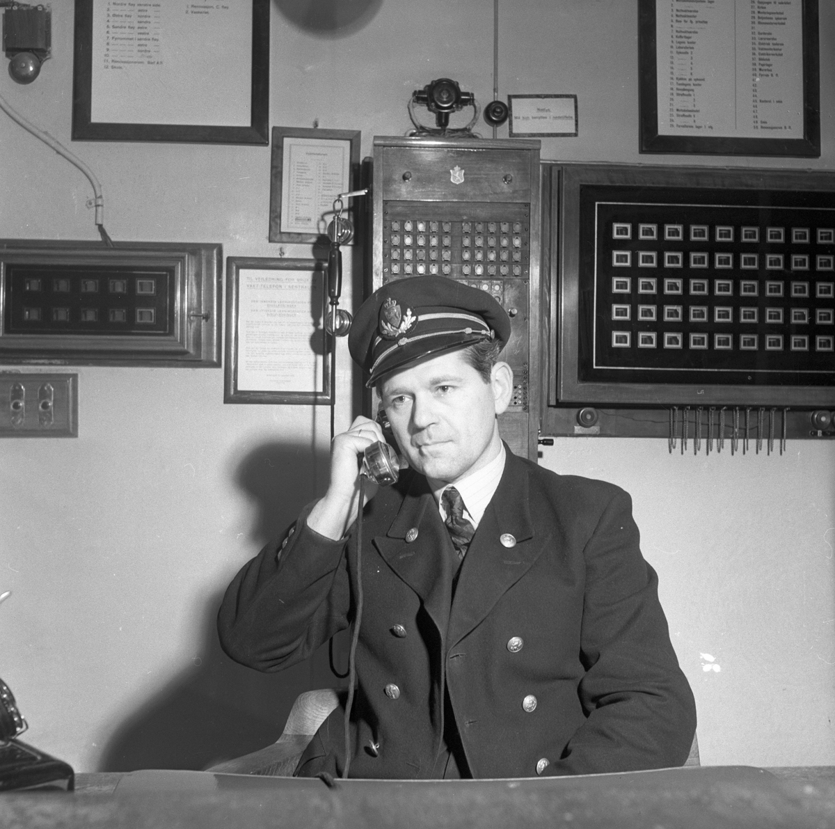 Mann i uniform snakker i telefon på kontor.
Fotografert 1951.