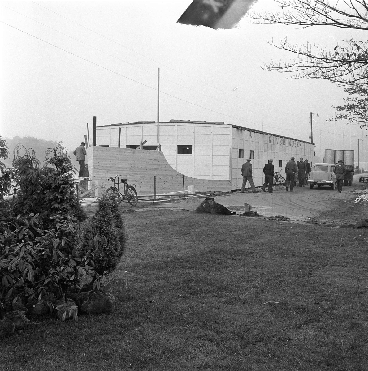 Blomsterutstilling, utstillingsområdet, bygning i bakgrunnen, flere menn samt bil foran bygningen, Fredrikstad,  03.10.1956