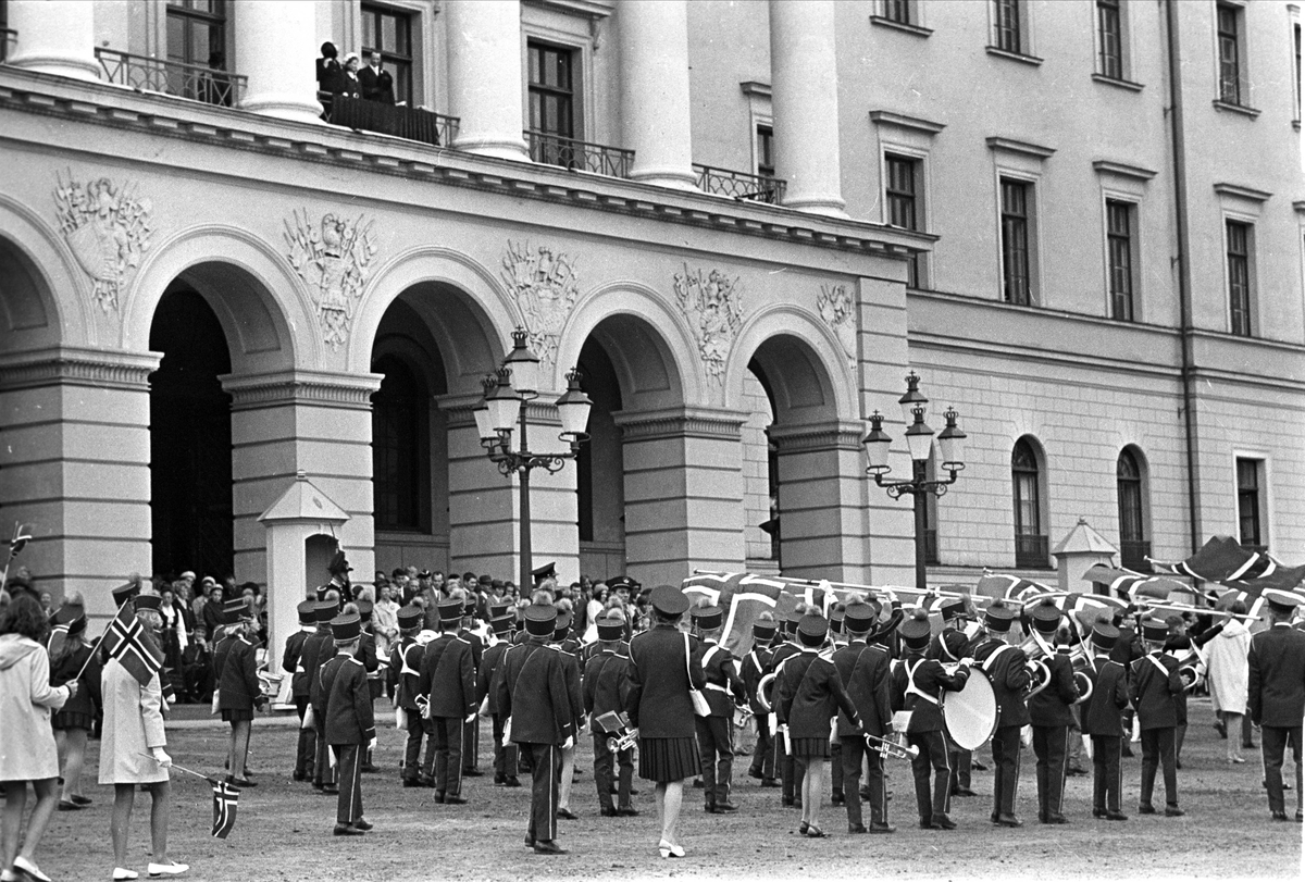 Fra Oslo, 17.05.1968. Musikkorps bak flaggborgen hilser kongefamilien den 17. mai.