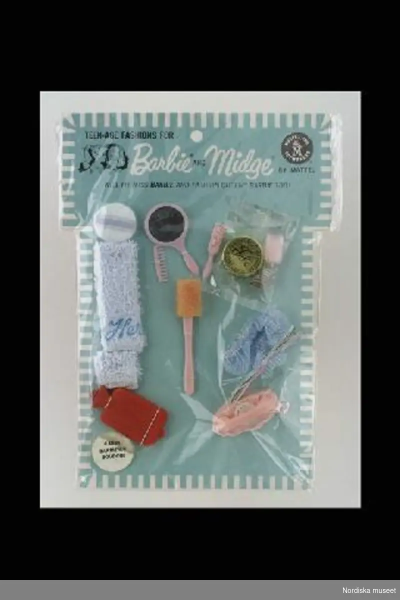 Inventering Sesam 1996-1999:
L 20  B 15 (cm)
Toalettillbehör till Barbie/Midgedocka, "Barbie's boudoir", i originalförpackning. Innehåller blå frott¿handduk och duschmössa,  kam, borste, spegel, badsvamp med handtag, rakapparat, och telefon av rosa plast, ask med talk, pudervippa och värmeflaska av rött gummi. 
Föremålen är fastsydda på grönblått pappark, täckt med plastfilm, text och bild i svart tryck. Modekatalog fasttejpad på baksidan.
Midge är dockan Barbie's bästa vän. 
Anna Womack feb. 1997