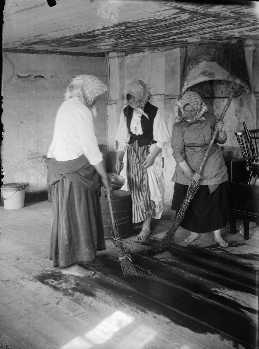 Hushåll. Tre kvinnor skurar golvet med kvastar ("sloror"). Bjurbäcken, Mangskog socken, Värmland.