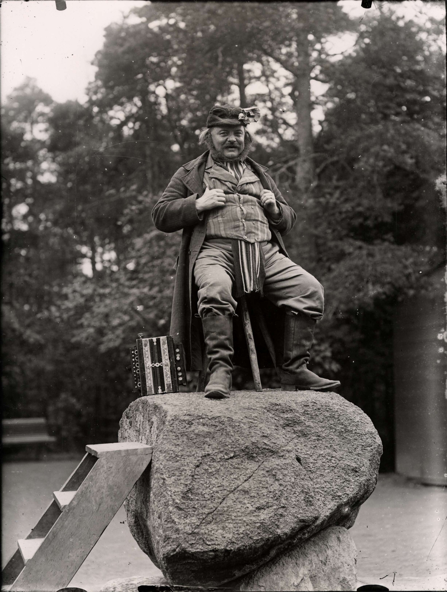 Jödde i Göljaryd (Karl Petter Rosén 1855-1900) poserar på Jödde-stenen på Skansen. Bredvid honom står ett dragspel.