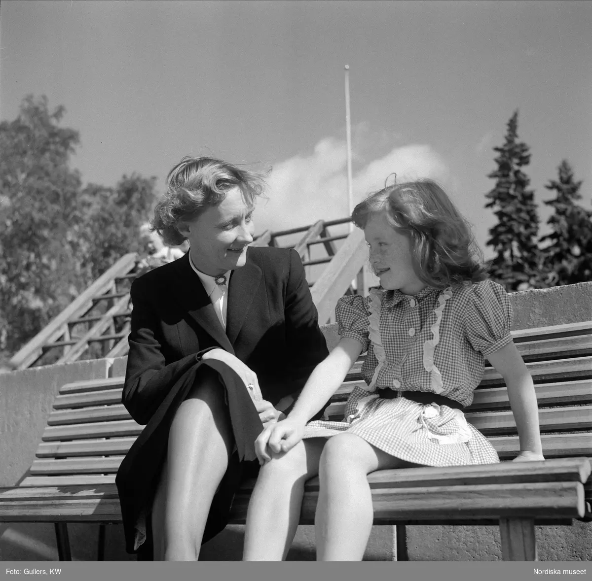 Astrid Lindgren sitter på bänk och pratar med flicka. 