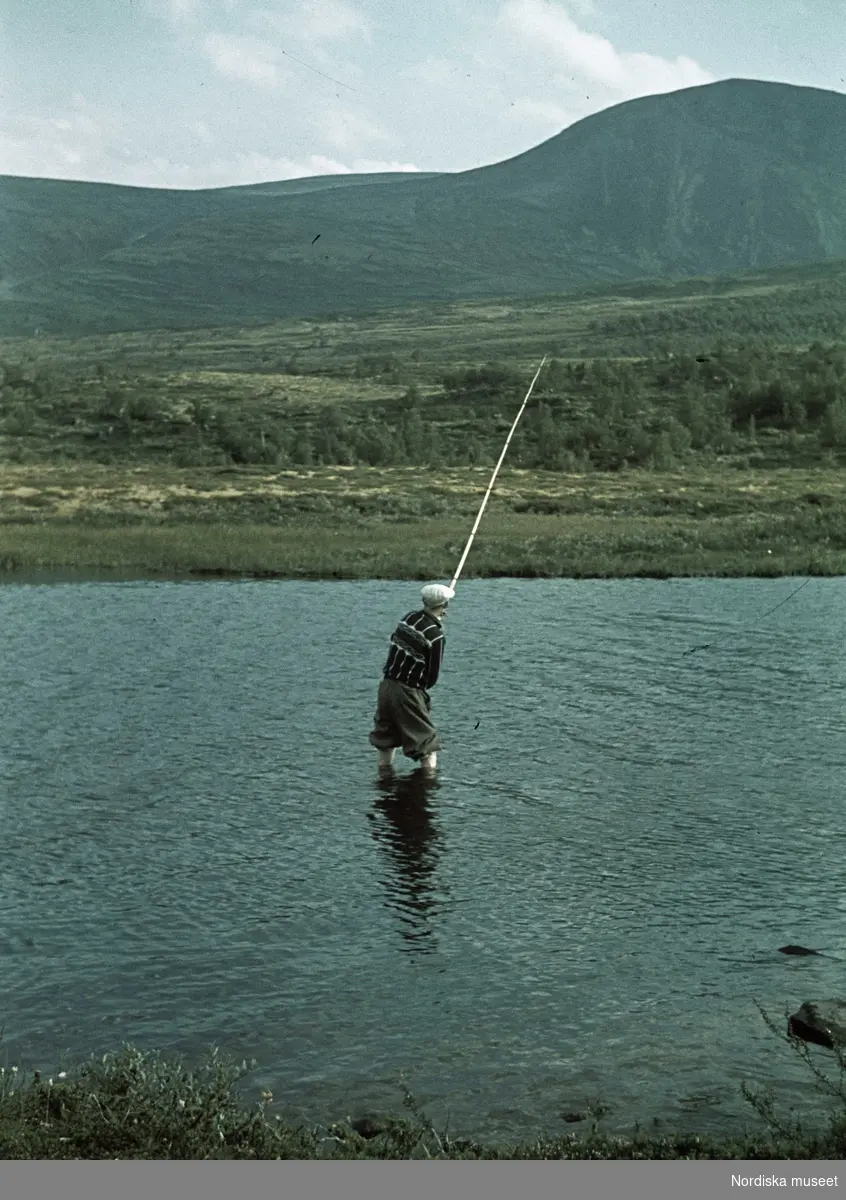 Landskap med en man som fiskar. I bakgrunden fjäll.