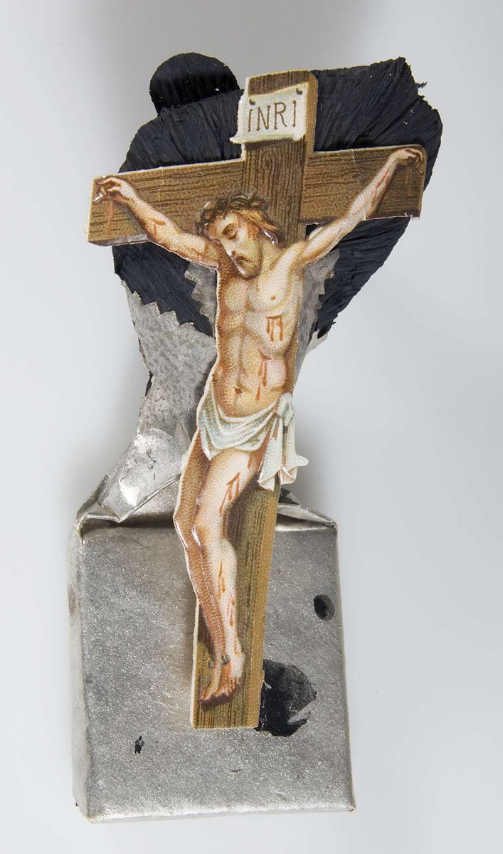Begravningskaramell, omslag av silverpapper. Frans av svart crêpepapper. Bild av korsfäste Kristus i färg.