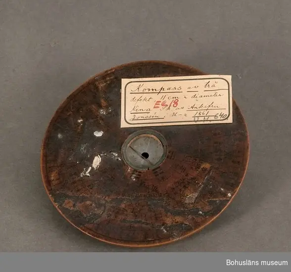 Ur handskrivna katalogen 1957-1958:
Kompass, defekt, Kina.
D.11,5 cm, Tj. 1,2 cm; svarvad av trä; i mittenett nålhus m. nål, m.m. av metall. Defekt.

Lappkatalog: 10