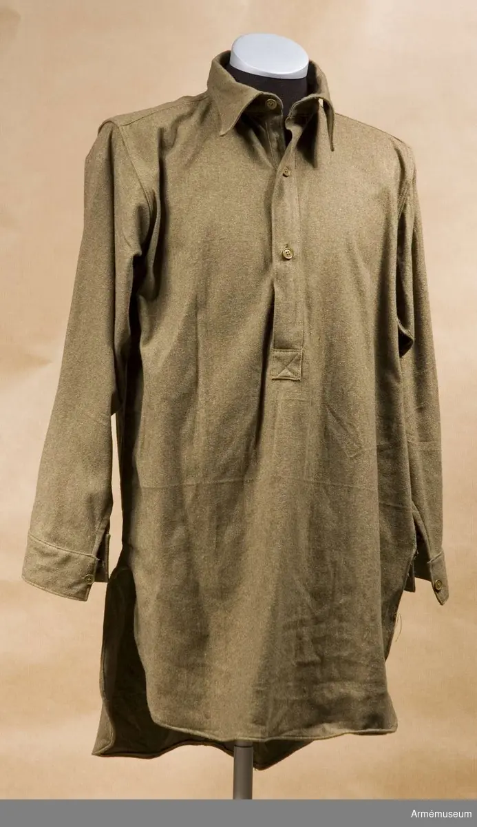 Grupp C I.
Skjorta med slips. Blusjacka i skjortform av khakityg. Knäppes vid bröstet med tre khakifärgade benknappar. Krage liggande. Ärmuppslag rakskurna med inskärning och en knapp. På blusens insida, vid kragen, fastsydd tygbit m stämpel "R. Elwood & Co Size 4, 1946"
