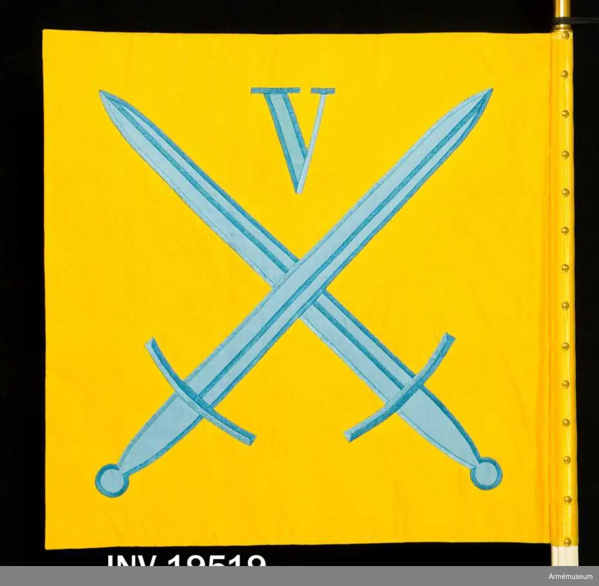 Kommandotecknet består av två tygsidor i gult siden. På sidenet finns i intarsia i blått siden två korslagda svärd och ovanför dessa i mitten en romersk siffra V, fem, även den i intarsia. Motivet finns på båda sidor. Kommandotecknet är spikat med 14 st tennlikor och ett ripsat band.

Samhörande nr AM 19519, 19520, standar, spets. 