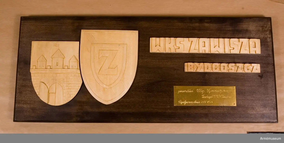 Minnesplakat i trä. Text på plaketten. Det finns två sköldar i trä fästade, en med en stadsport som motiv, troligen Bydgoszczs stadsvapen, och den andra ett "Z", för Zawisza.
1974.