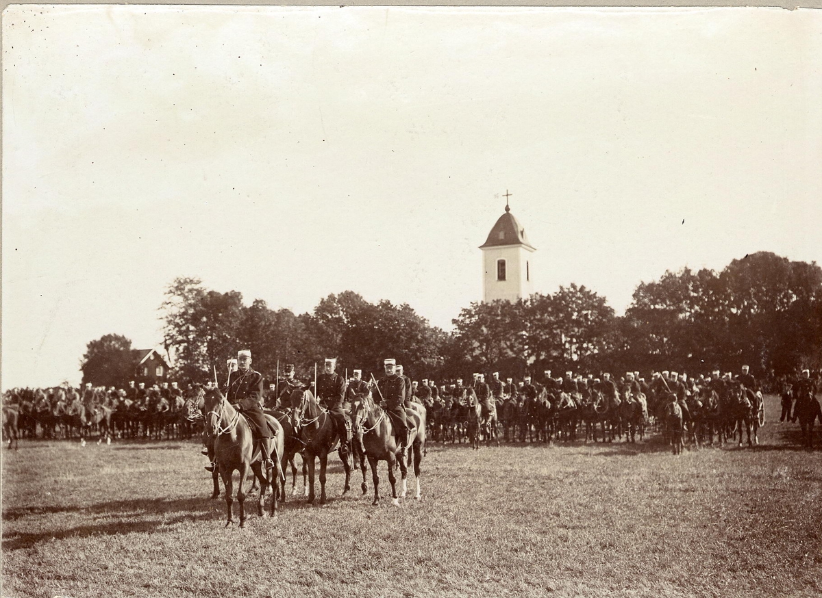 Kavalleritrupp med befäl i täten uppställd framför kyrka.