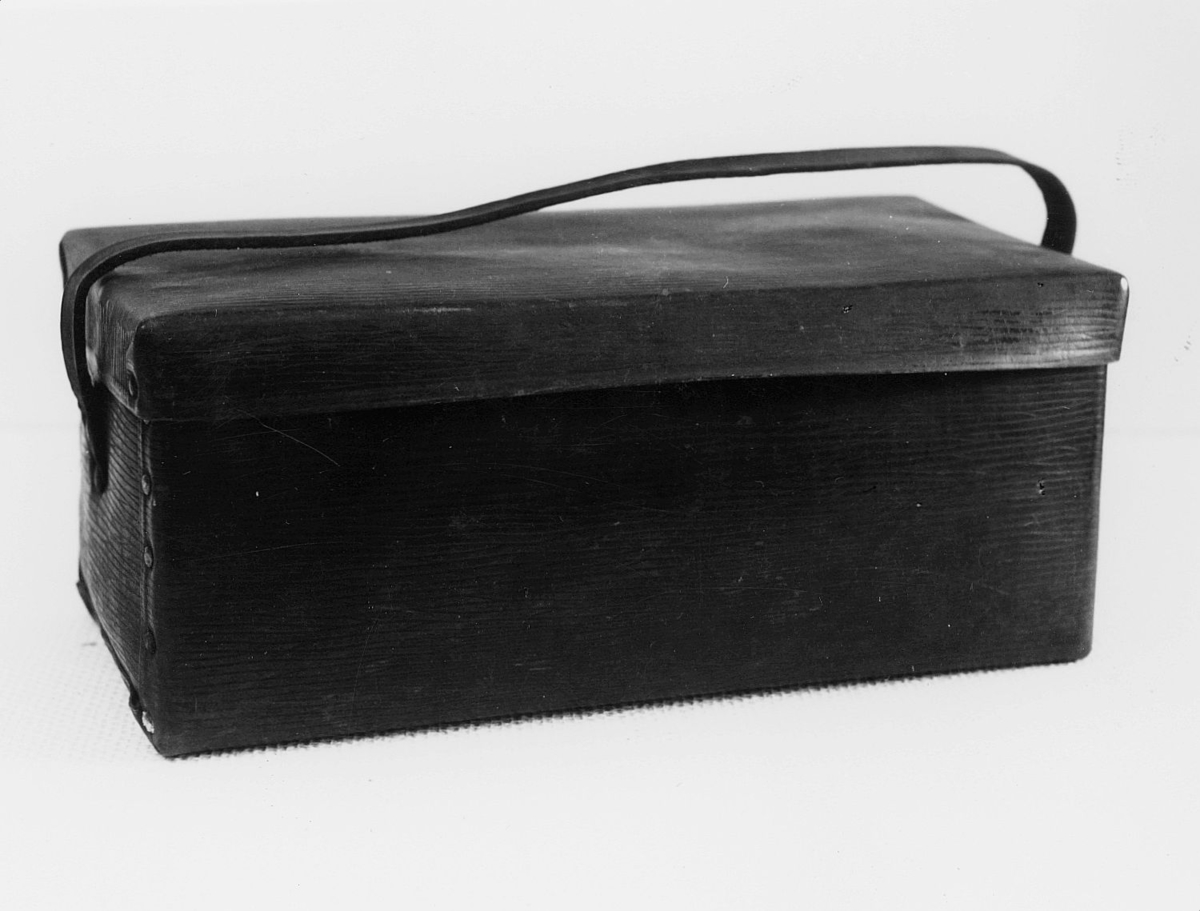 Väska, s k unicabox. Rektangulär låda med lock och bärrem av mörkbrunt konstläder. Egentillverkad låspinne av trä. Använd som matväska under tiden 1920 - 1946.

Vulkaniserat lumppapper: unicafibern