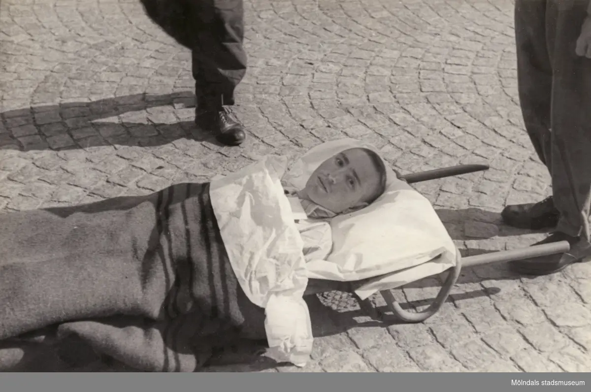 "Karantänsförläggning" på Kvarnbyskolan för överlevande från koncentrationsläger i Tyskland och Polen 1945.  
Skolan fungerade under denna sommar som beredsskapssjukhus.

En ung man på bår.