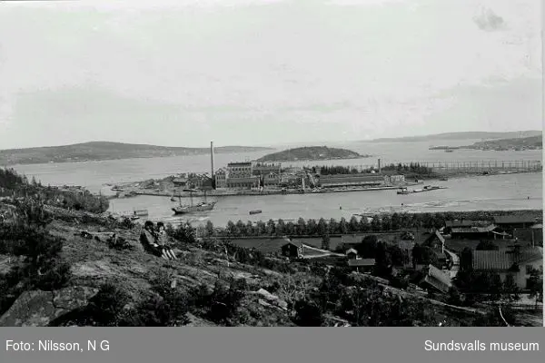 Vy över Killingholmen med Ortvikens sulfitfabrik till vänster, massamagasin samt ångsågen till höger. Tjuvholmen ses bakom.
