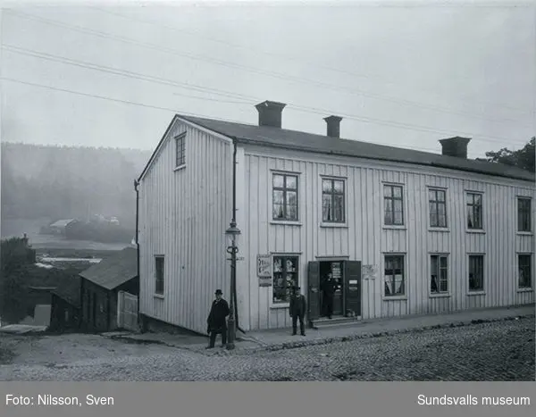 Salanderska gården, Storgatan väst på stan. Vid lyktstolpen står disponent Albert Fridner, vid Sundsvalls Ölbryggeri, verksam åren 1895-1912. I gränden till ån vattnades bryggerihästarna.