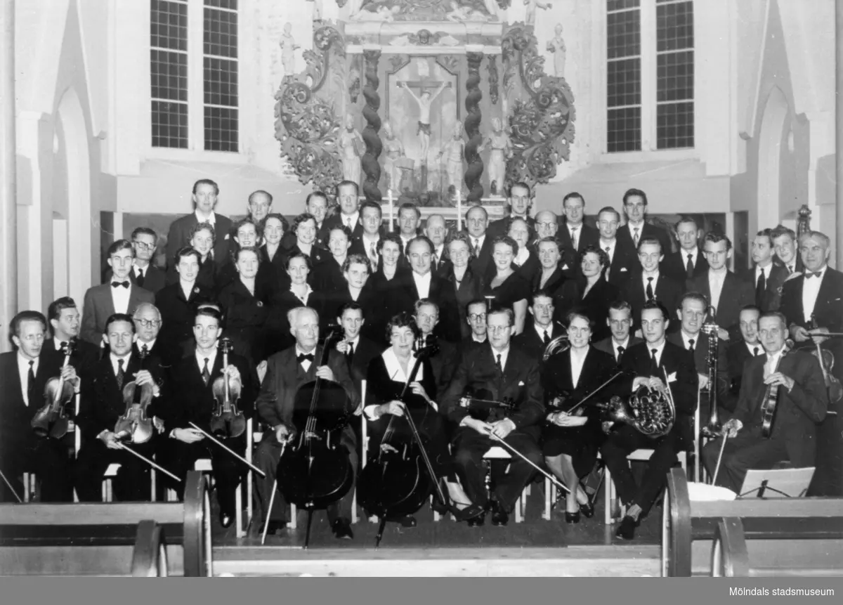 Mölndals körsällskap (dirigent: Lennart Hillman) sittande respektive stående framför altaret i Fässbergs kyrka, 1955. Okänd orkester.