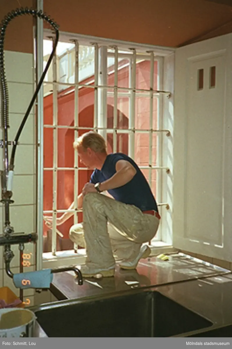 En man som målar ett fönster inomhus på Gunnebo slott.