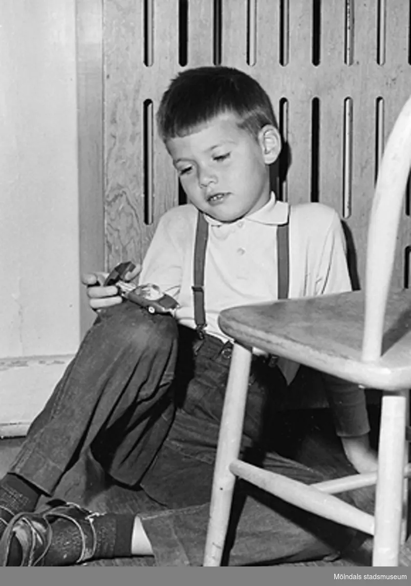 En pojke sitter på golvet hållandes en leksaksbil i handen. Holtermanska daghemmet 1953.