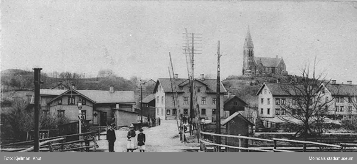 Järnvägsövergången på Kvarnbygatan, i bakgrunden Mölndalsbro och Fässbergs kyrka. Man ser fastigheterna Kungsbackavägen 1 samt Göteborgsvägen 1, 3 och 5. 
Vid vänstra gaveln av Göteborgsvägen 1 ses Villa Björkås (Frölundagatan 25B). 
Spårvagnshallarna är ännu inte byggda, så fotot togs innan 1907.