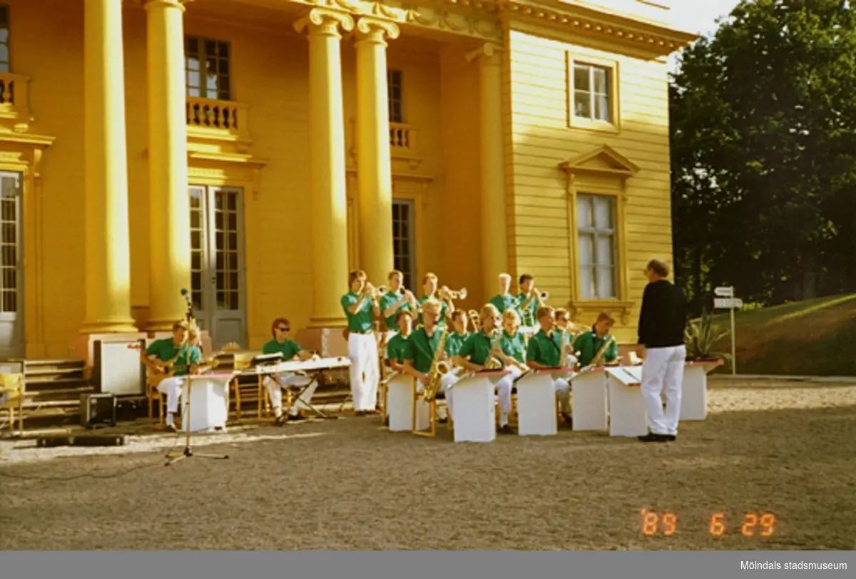 Vy från nordost på musikunderhållning av ungdomsorkester som pågår framför slottet. Musikerna är iklädda vita byxor och gröna tröjor.