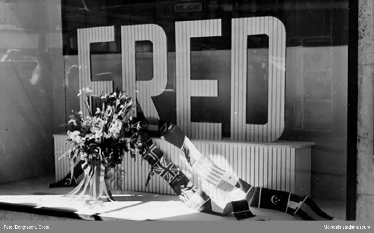 Vi firar FREDEN, åker in till Göteborg och lunchar på Gillblads, år 1945. Orden FRED och blomsteruppsättning i ett skyltfönster.
Laboranter från SOAB-Svenska Oljeslageri AB, Kvarnbygatan i Mölndal. Relaterade motiv: 2004_0032 - 0035.