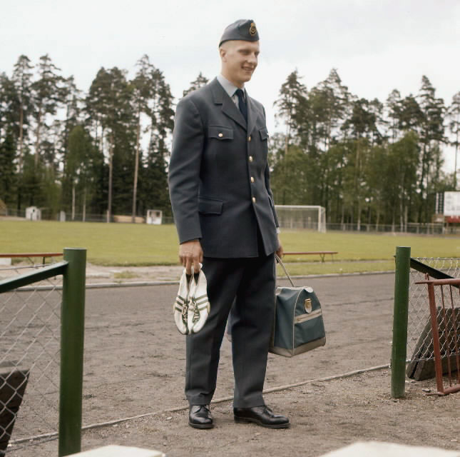 Brevbärare i uniform modell 1962, fotograferad på en idrottsplats med spikskor i höger hand och en väska i vänster.