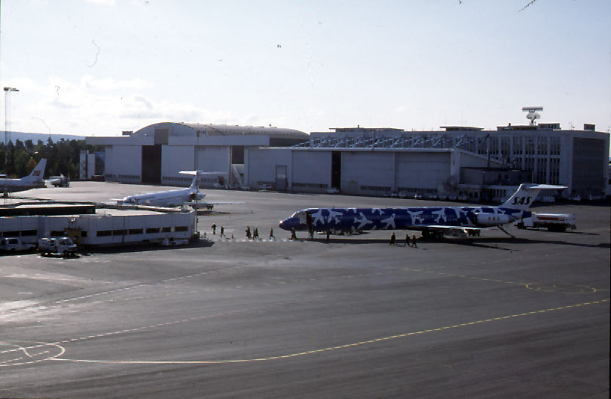 Lufthavn, flere personer foran 1 fly på bakken, MD-82, LN-RMD "Fenge Viking" fra SAS.  2 andre fly og 1 hangarbygning fra SAS i bakgrunnen.