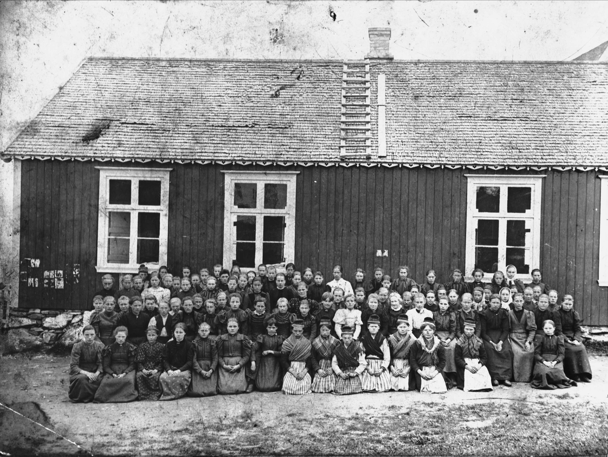 Gruppebilde av konfirmantkull, fotografert utenfor "kirkestua" på Trondenes. I midten av første rekke sitter flere jenter med samedrakter.