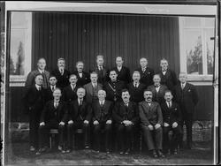 Gruppe, menn utenfor en bygning. Skiptvet. 
UKjent år.